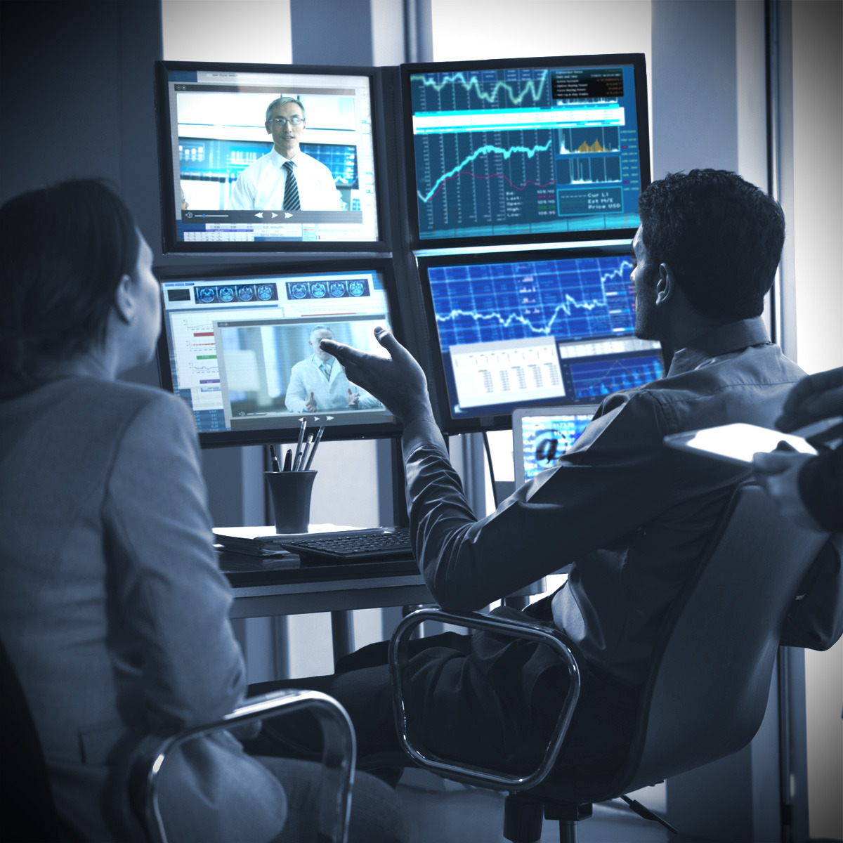 Two professionals reviewing multiple screens of financial data