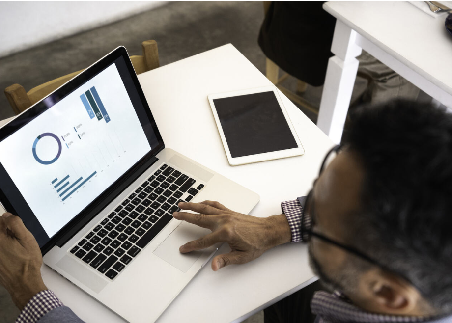 A man works on a laptop. Data graphs can be seen on the screen