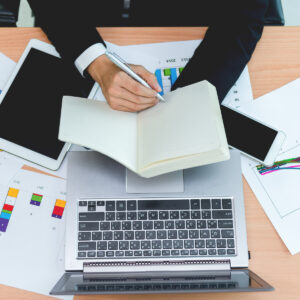 A man writing in a notepad over a laptop